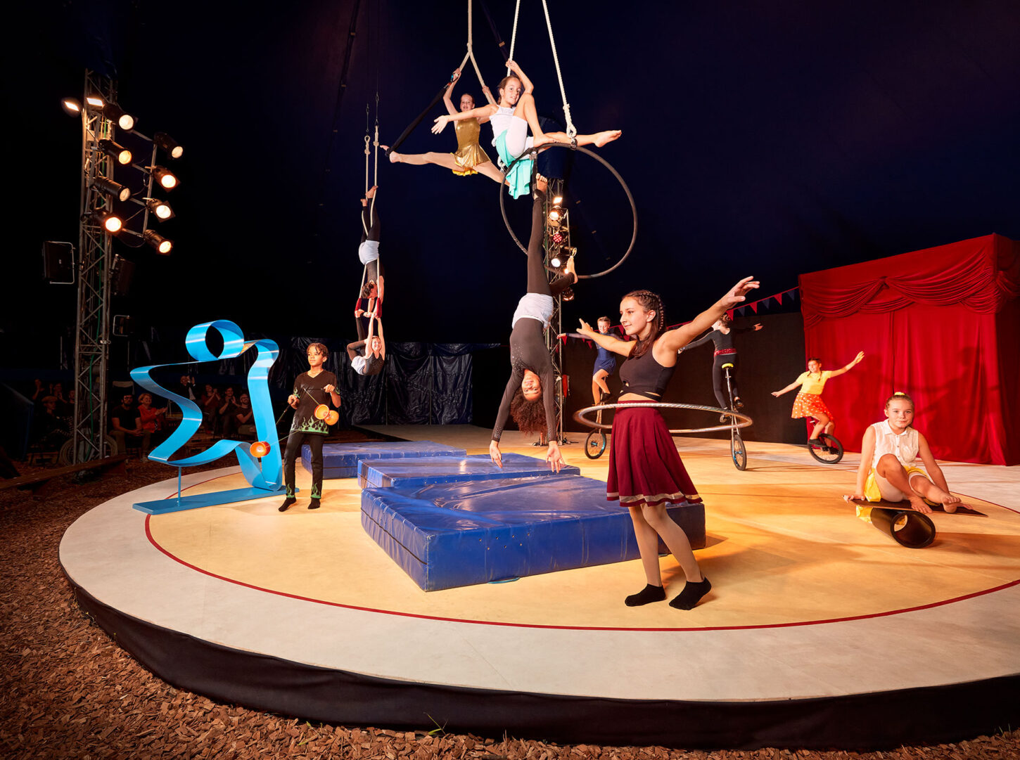 Das menschengrosse blaue Stiftungslogo aus Metall steht vorne auf der Zirkusbühne, auf der etwa zehn Kinder ihre Zirkuskunststücke aufführen.